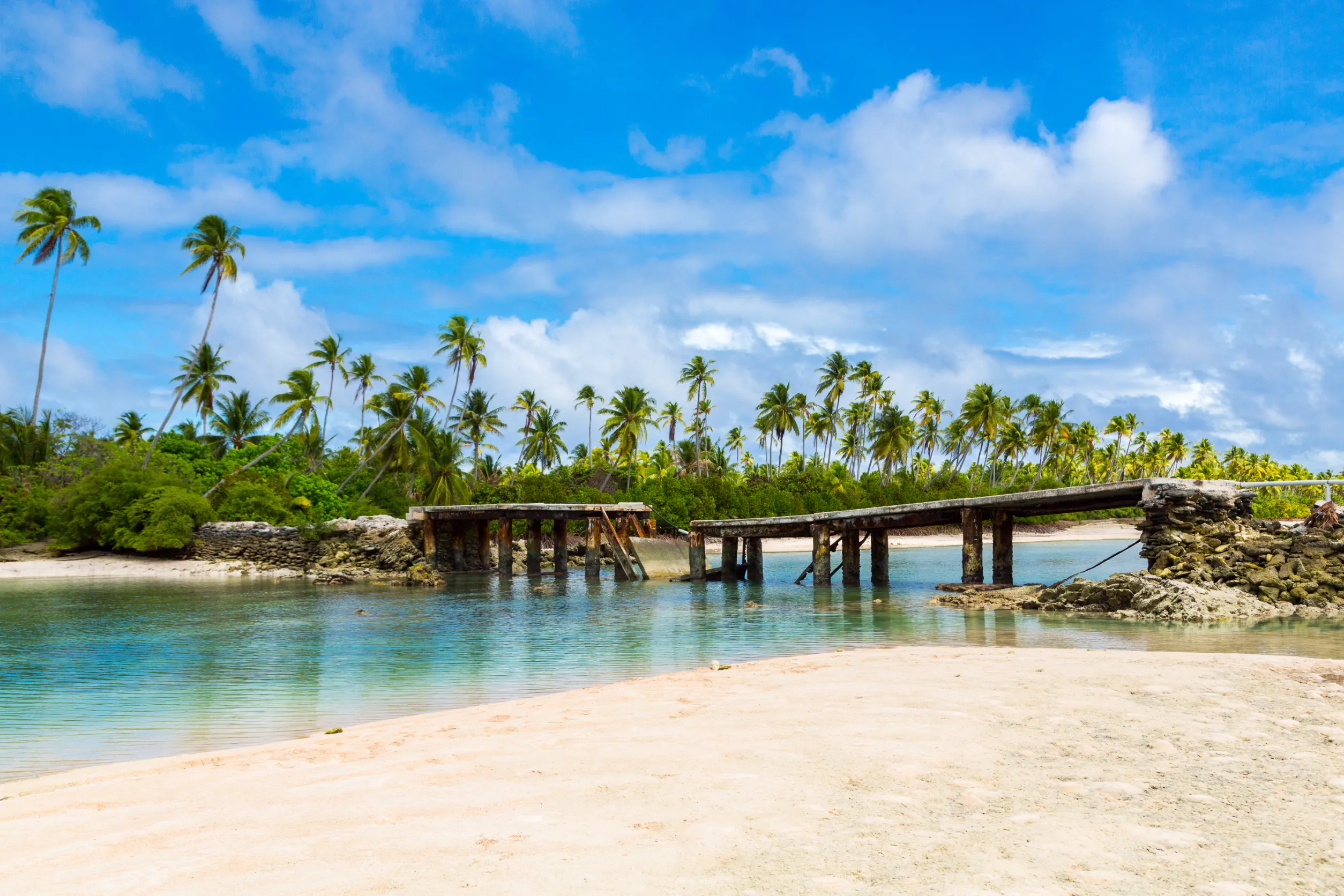 broken bridge under palm trees between islets over lagoon